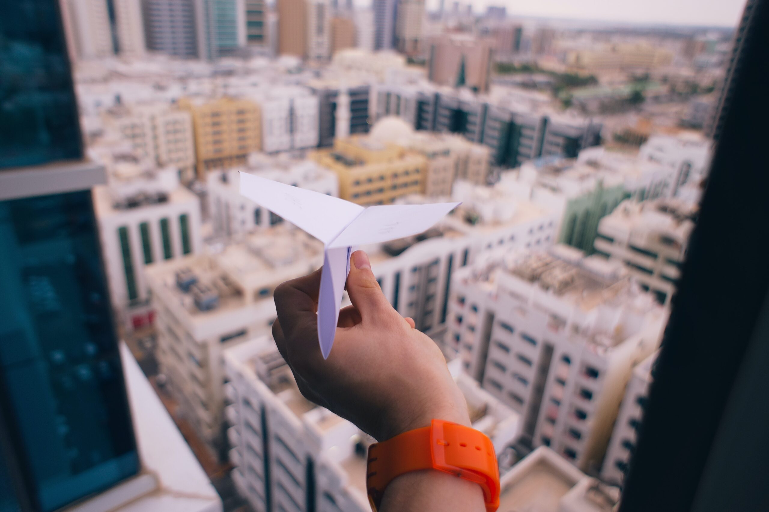 A hand holding a paper airplane with a city in the background